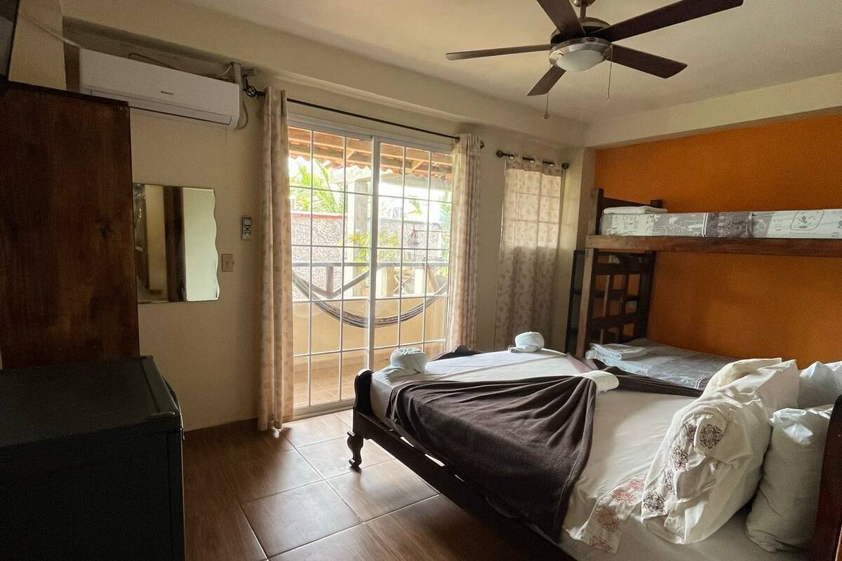 A hotel room with a bed, a ceiling fan, a window with curtains, and a wooden wardrobe.