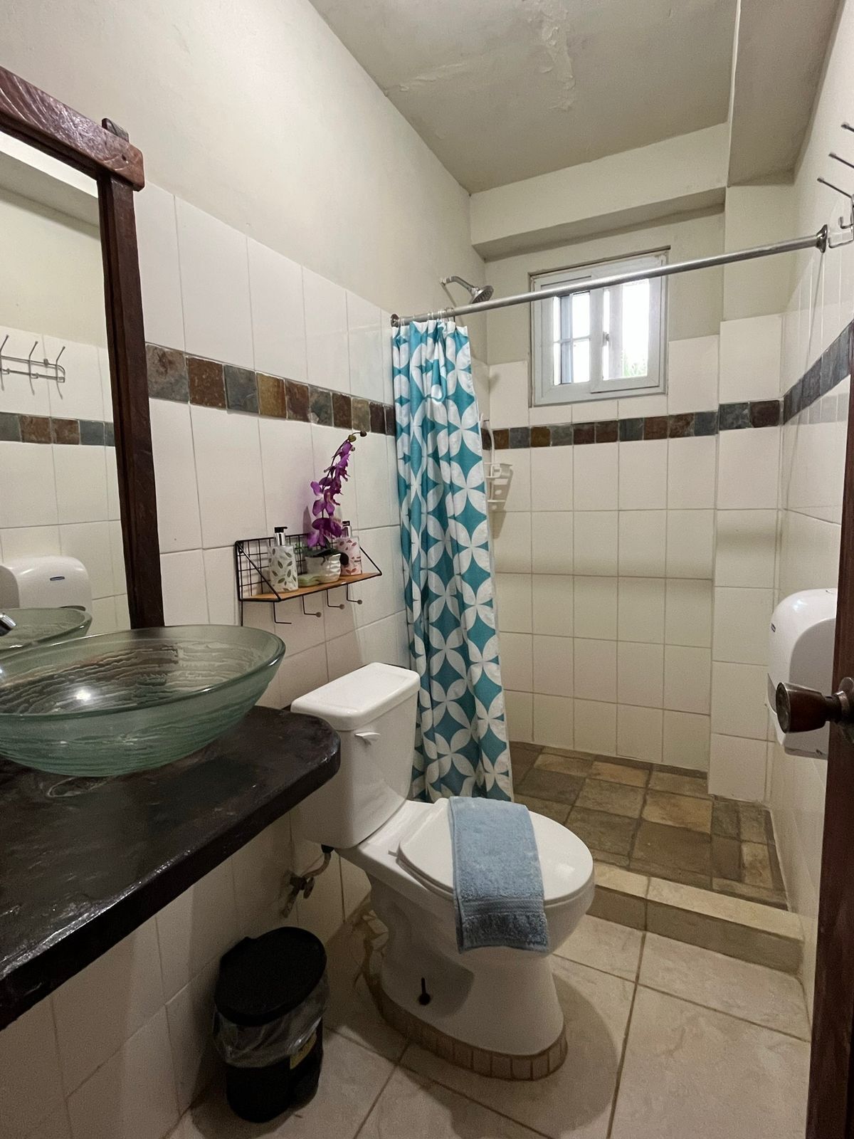 A bathroom with a glass bowl sink, a toilet, a shower curtain, and a window.