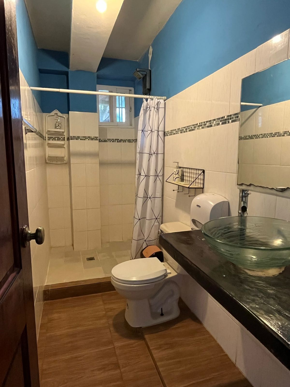 Un baño con inodoro, lavamanos de vidrio, ducha y toallero.