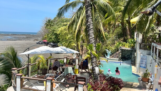 A pool area with lounge chairs and umbrellas, surrounded by palm trees and a view of the beach. - Hotel y Restaurante Mama Ines (Hicaco)