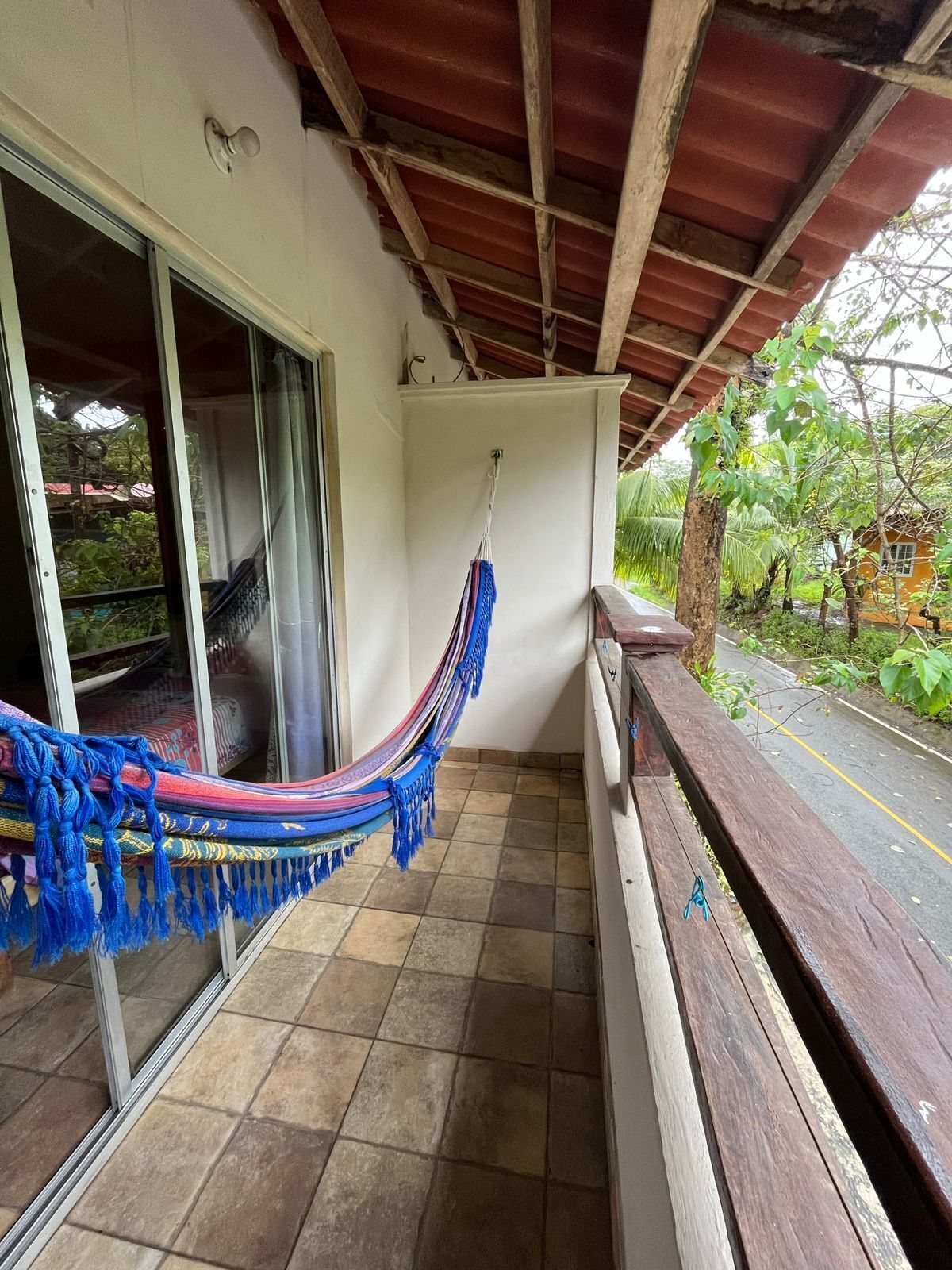 A hammock on a balcony with a view of a road and greenery.