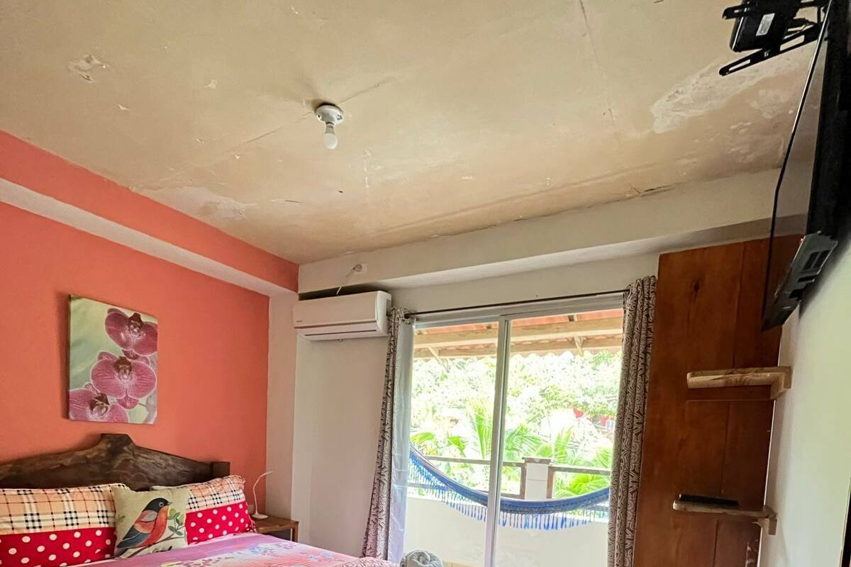 A bedroom with a bed, an air conditioning unit, a wooden wardrobe, and a sliding glass door leading to a balcony.