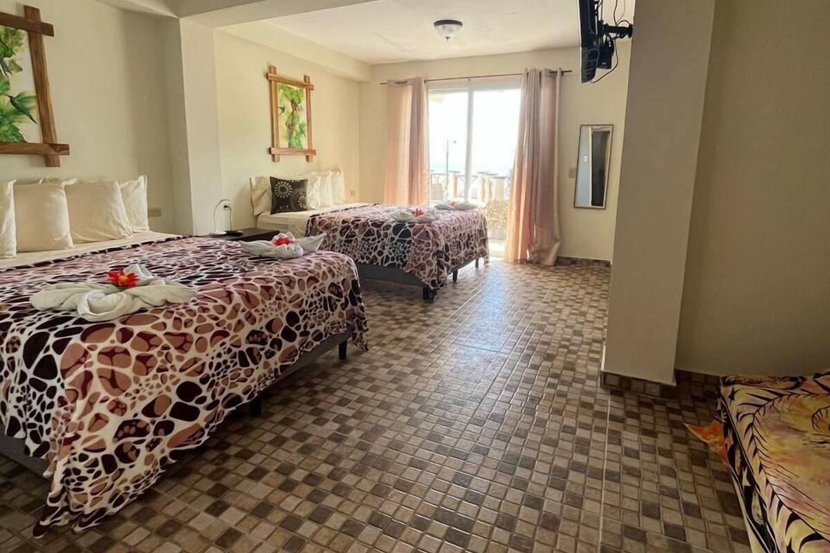 A hotel room with two beds, a large window with curtains, a tiled floor, and a ceiling light.