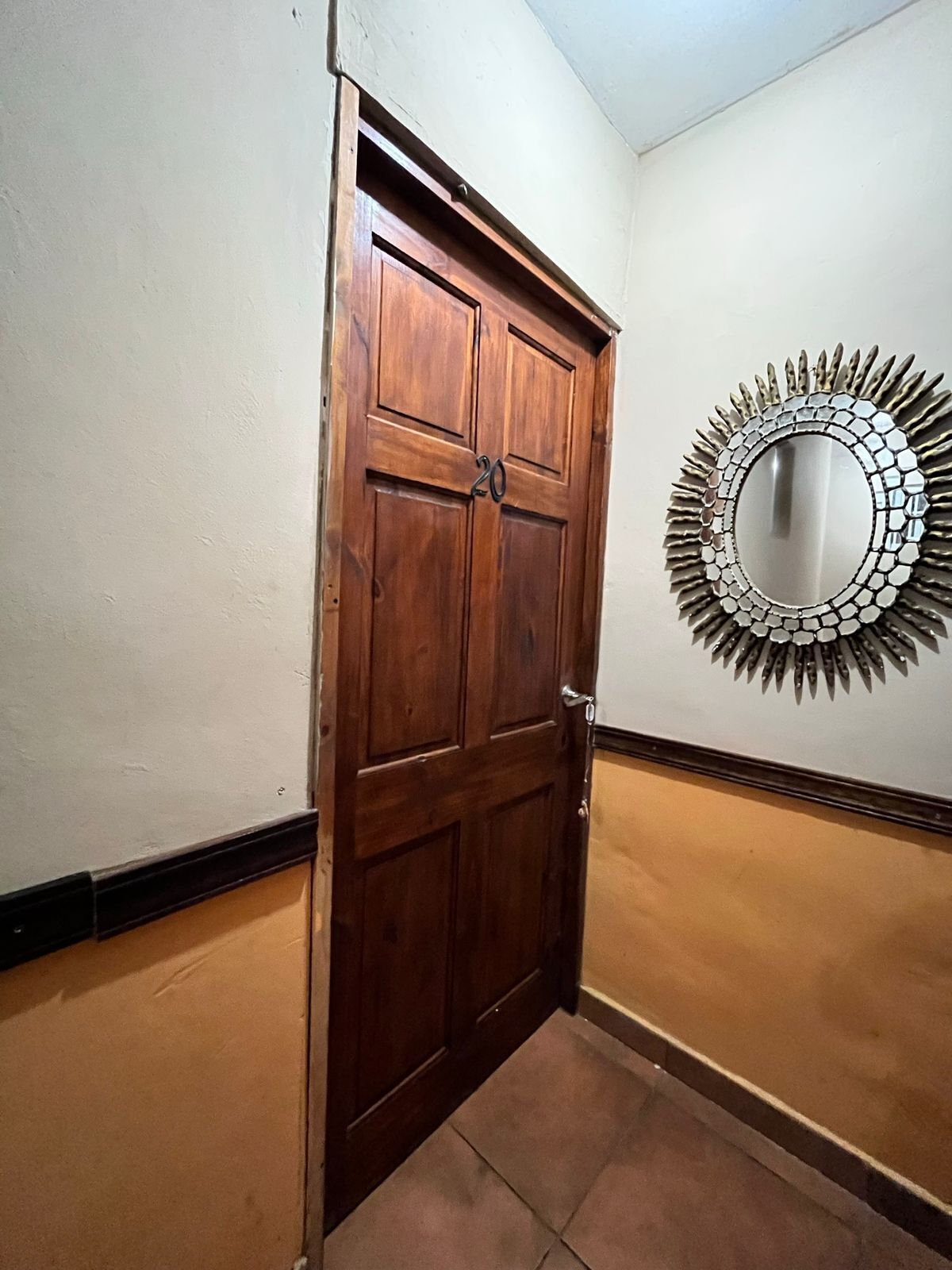 A wooden door with a number '20' and a mirror with a sunburst design on the wall.