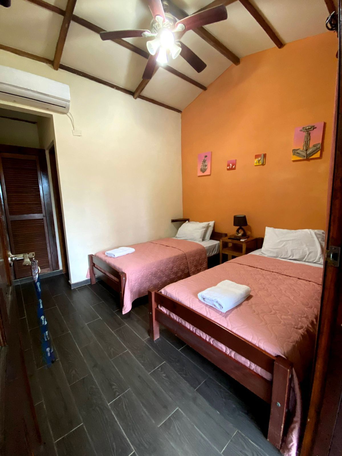 A hotel room with two single beds, a ceiling fan, and artwork on the walls.