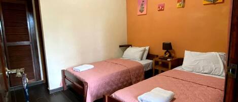A hotel room with two single beds, a ceiling fan, and artwork on the walls.