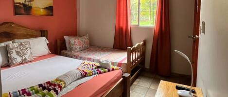 A bedroom with two beds, a desk, a chair, a window with curtains, and an air conditioning unit.