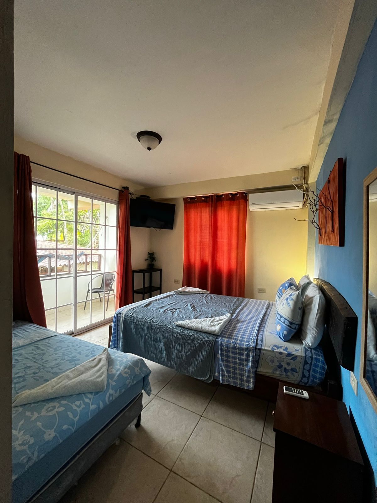 Habitación de hotel con dos camas, televisión, ventilador de techo y puerta corrediza de vidrio al exterior.