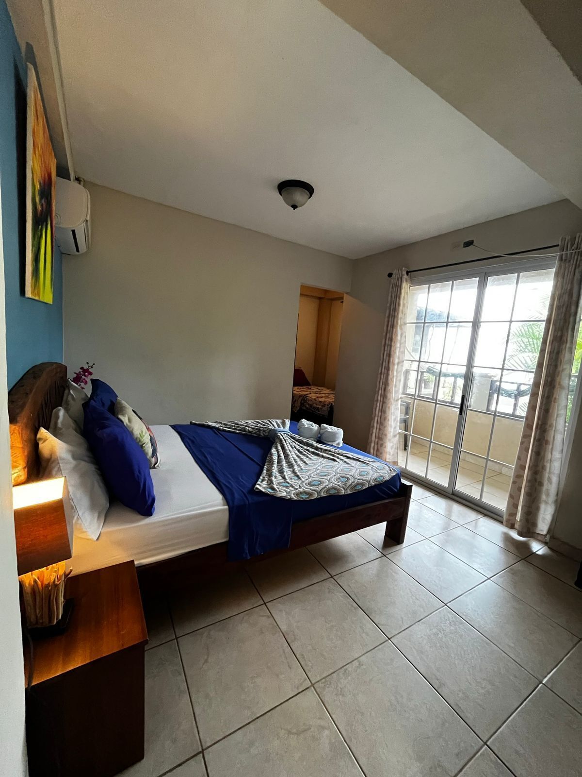 A bedroom with a bed, a desk, a chair, a window with curtains, and a view of the outside.