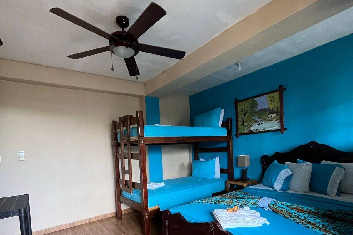 A room with a bunk bed, a single bed, a ceiling fan, and a painting on the wall.