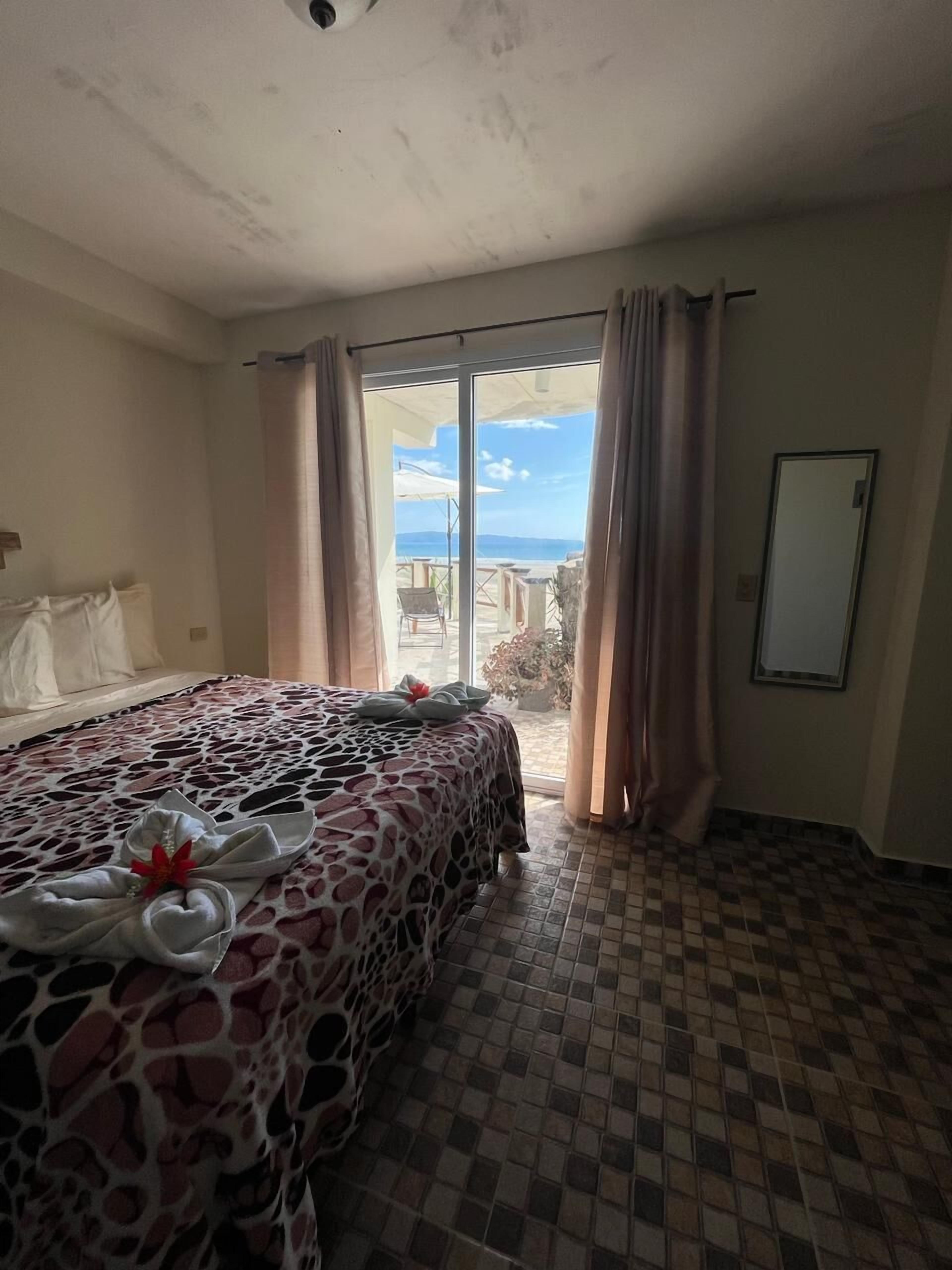 A hotel room with a bed, a large window, and a view of the outdoors.