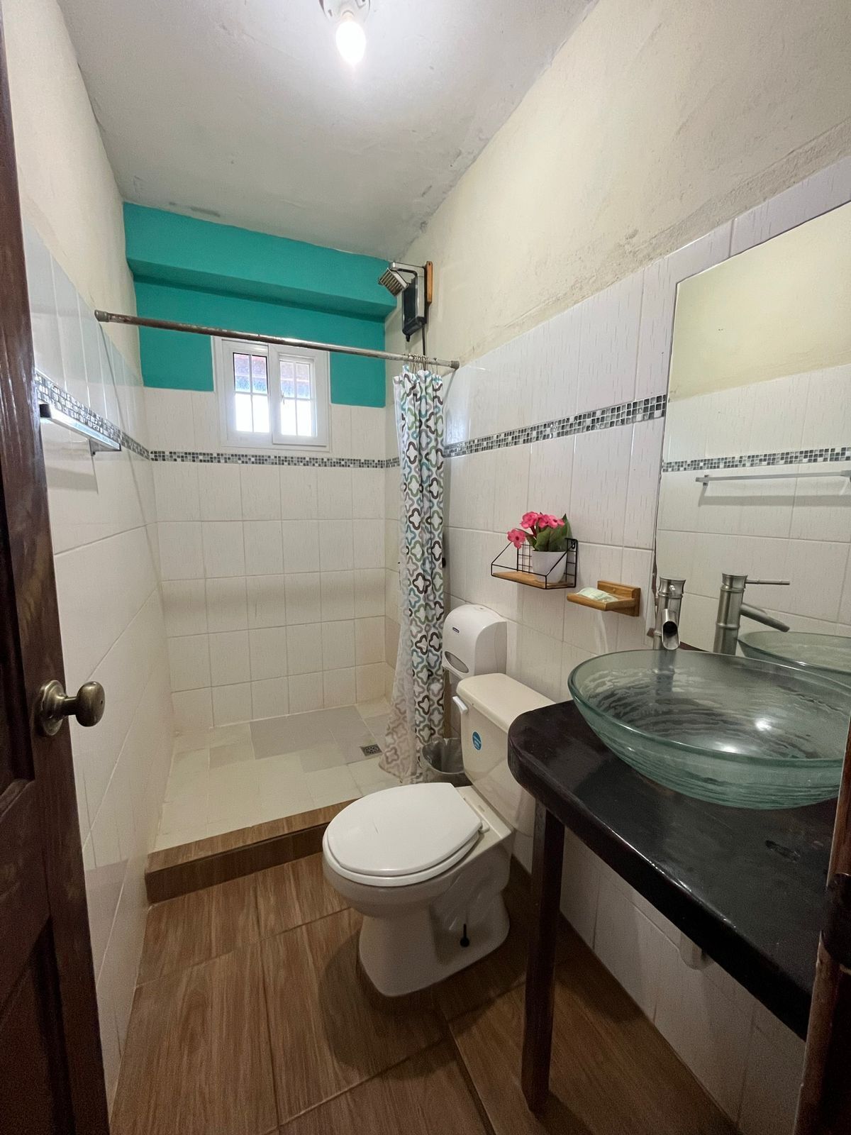 A bathroom with a glass sink, white toilet, and shower area.
