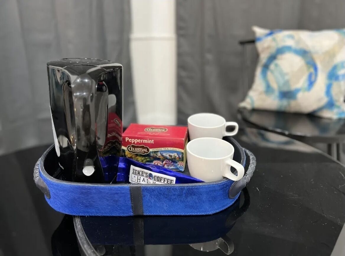 A tray with a coffee maker, a box of peppermint tea, and two white cups on a black table.