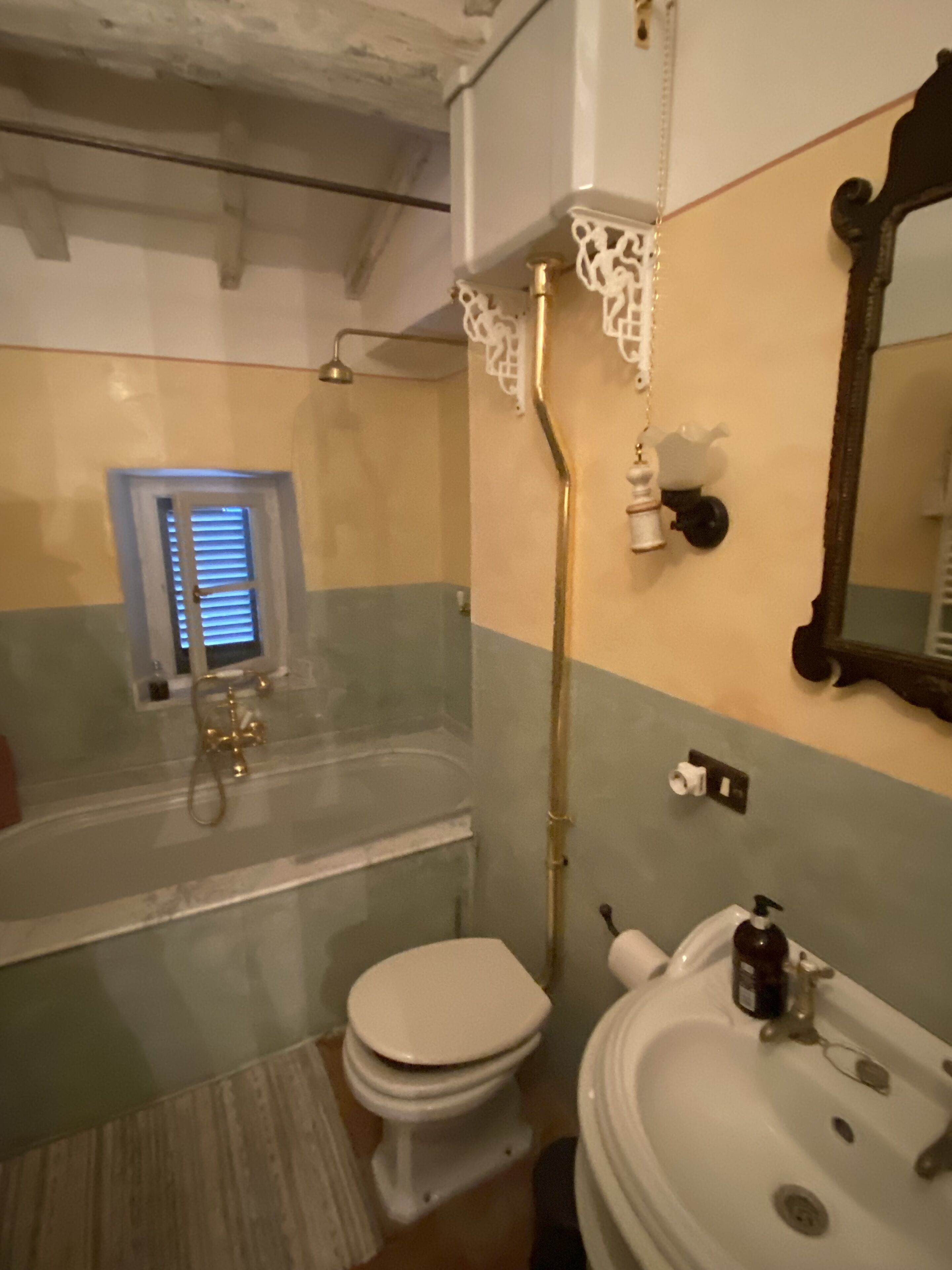 Une salle de bain équipée d’une baignoire, de toilettes, d’un lavabo et d’une fenêtre avec des stores.