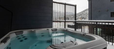 A hot tub on a balcony with a view of a snowy landscape and a building in the background.