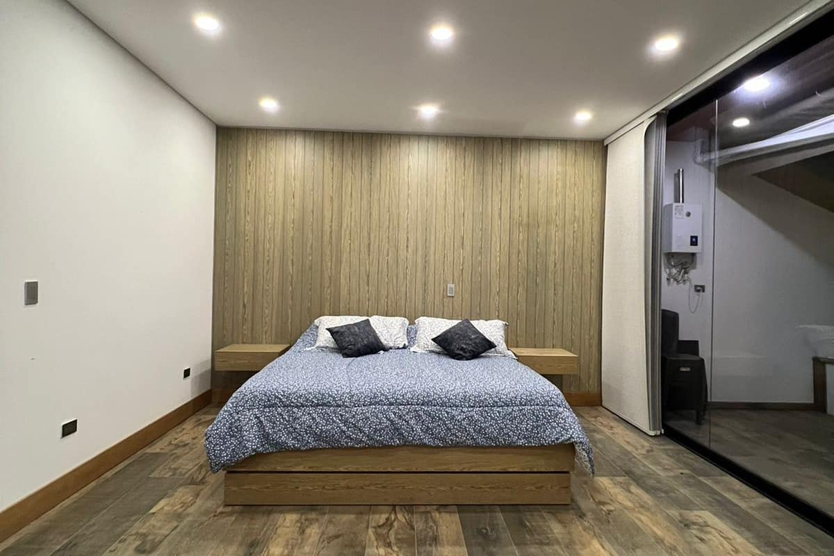 Une chambre à coucher moderne avec un plancher en bois, un lit recouvert d’une couvre-lit à motifs et un panneau mural en bois.