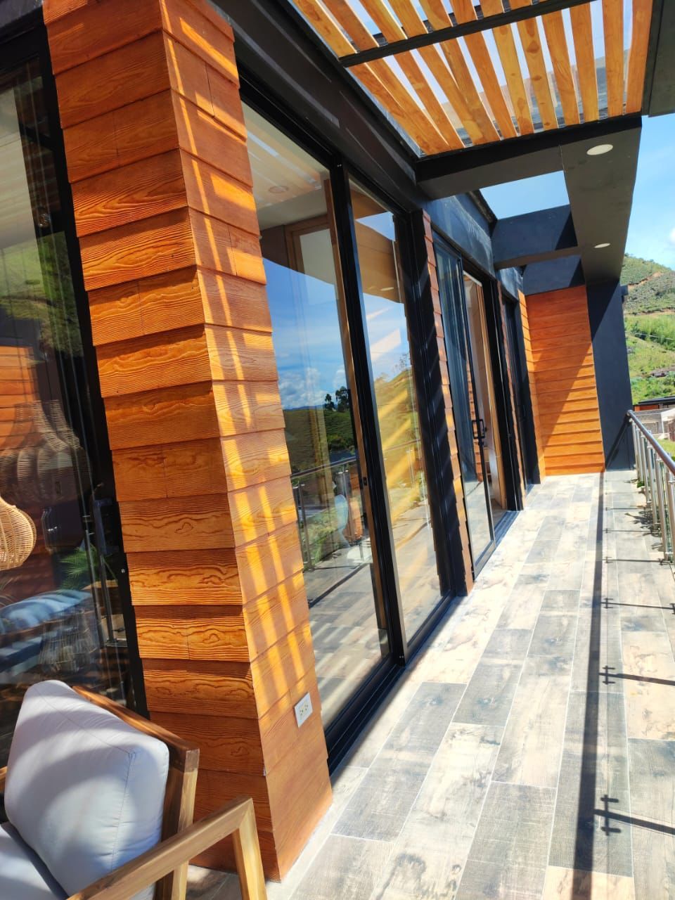 A modern building with large glass doors, wooden paneling, and a covered outdoor area with a view of the landscape.