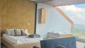 Un dormitorio moderno con una cama grande, una zona de comedor con mesa y sillas, y vistas al paisaje a través de un ventanal.