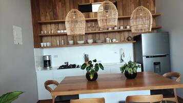 A modern kitchen with wooden cabinets, a central island with chairs, and hanging wicker light fixtures.