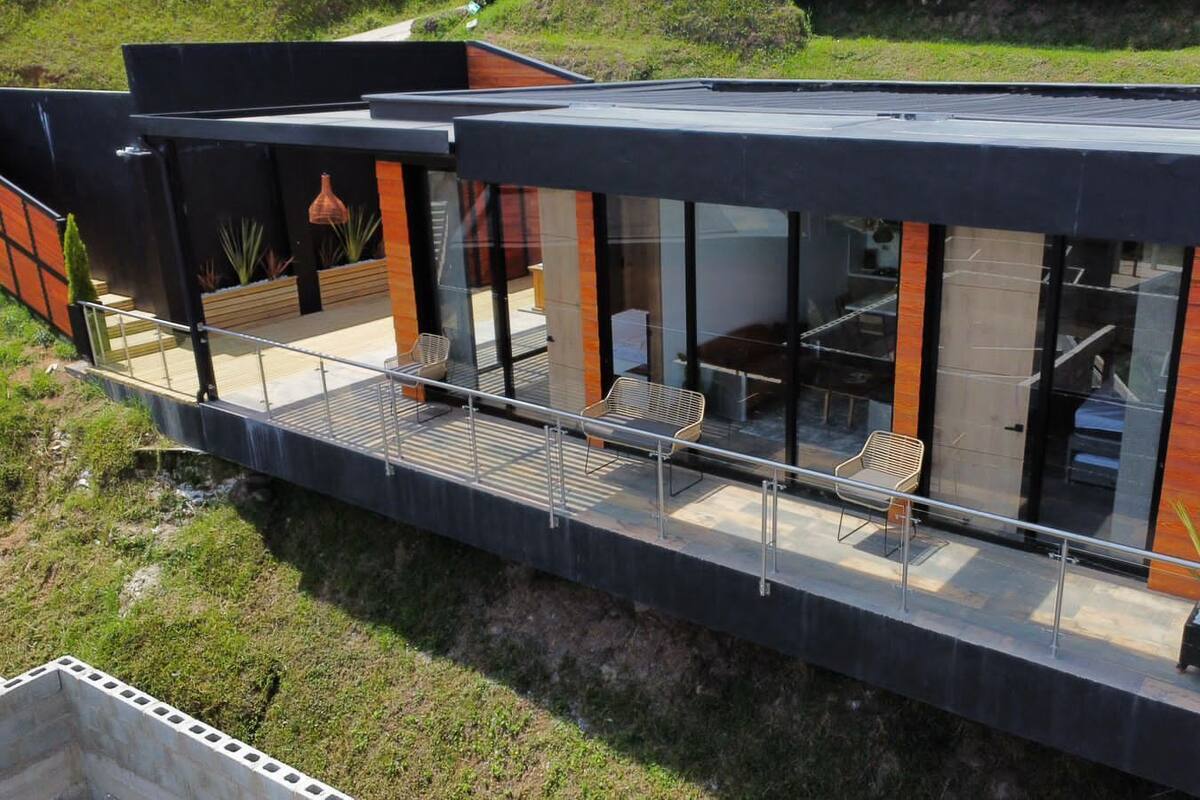 Une maison moderne dotée d’un balcon en verre, d’un espace salon extérieur et offrant une vue sur le paysage environnant.