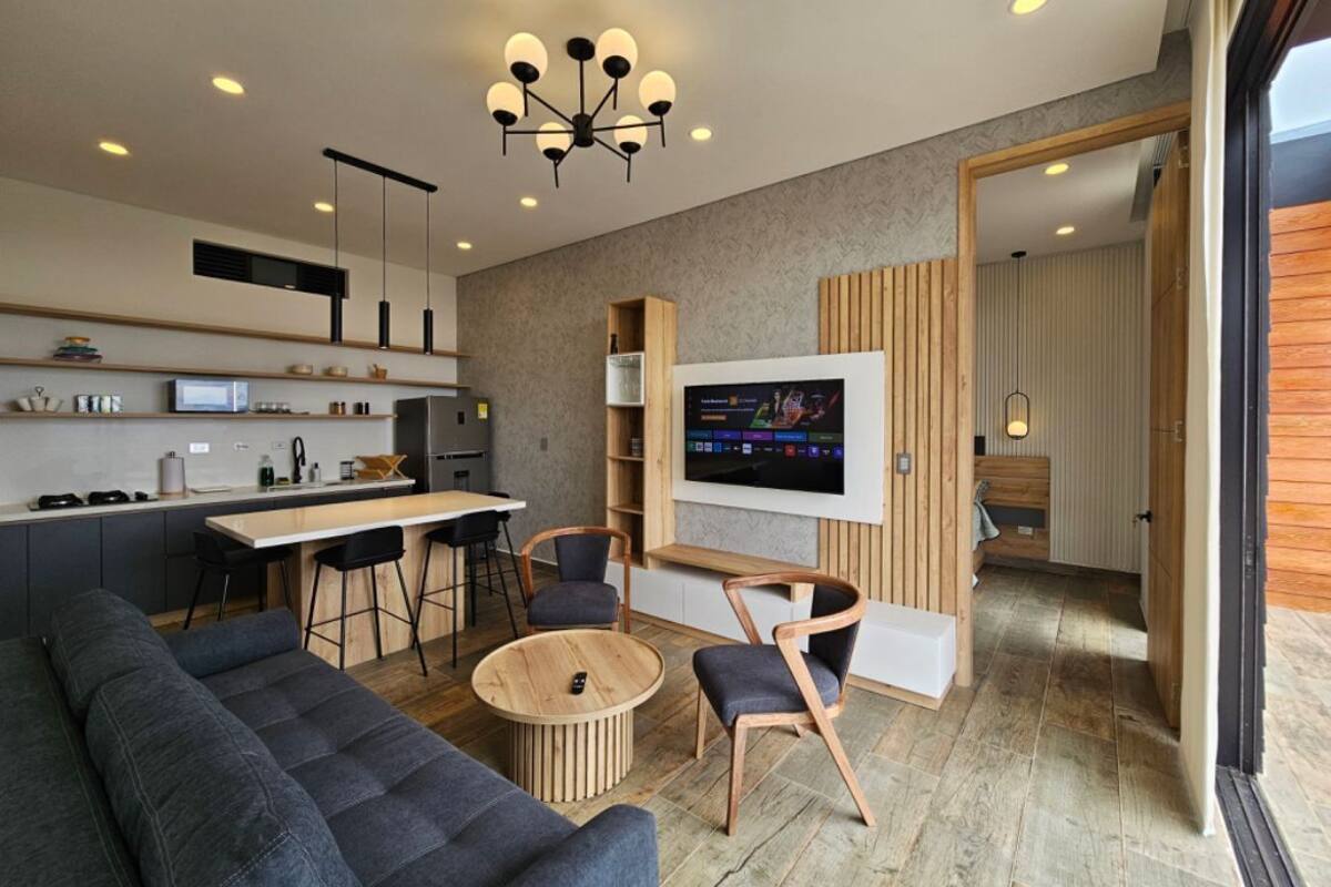 Une cuisine moderne avec un coin repas, un téléviseur fixé au mur et un espace salon confortable avec un canapé et des fauteuils.