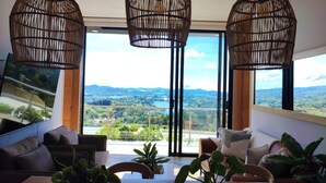 A modern living room with a large window offering a scenic view of mountains and greenery. - MONTECIELO HOSTING GUATAPE (El Peñol)