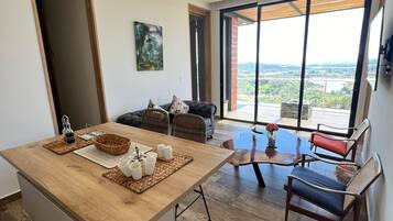 Una cocina moderna con una isla de madera, una zona de comedor con mesa de vidrio y vistas a un paisaje a través de ventanas amplias.
