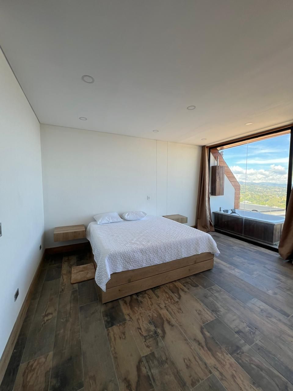 Un dormitorio moderno con una cama grande, piso de madera y vistas a través de un ventanal corredero.