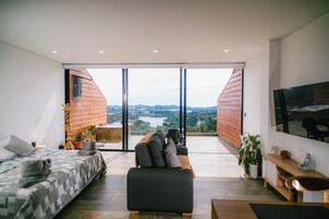 Una sala moderna con un ventanal grande, un sofá, una cama y un televisor.