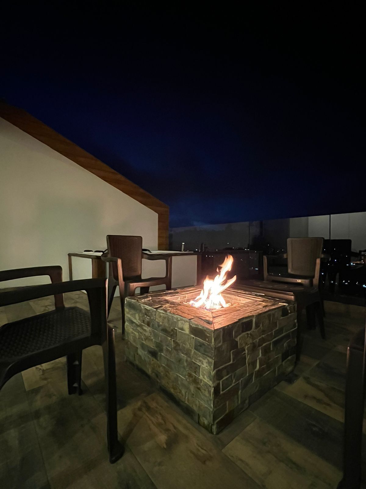 A stone fire pit with chairs around it, set against a dark sky.