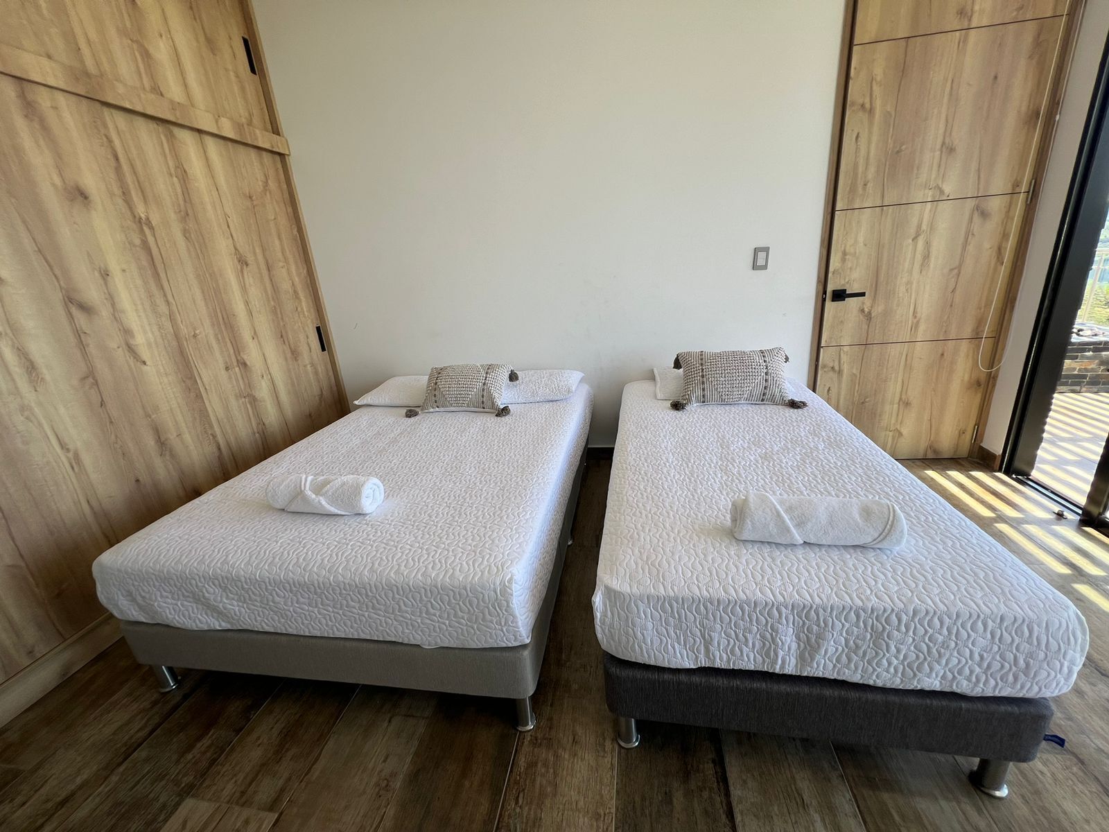 Two single beds with white bedding and towels, a wooden floor, and a large window with a view.