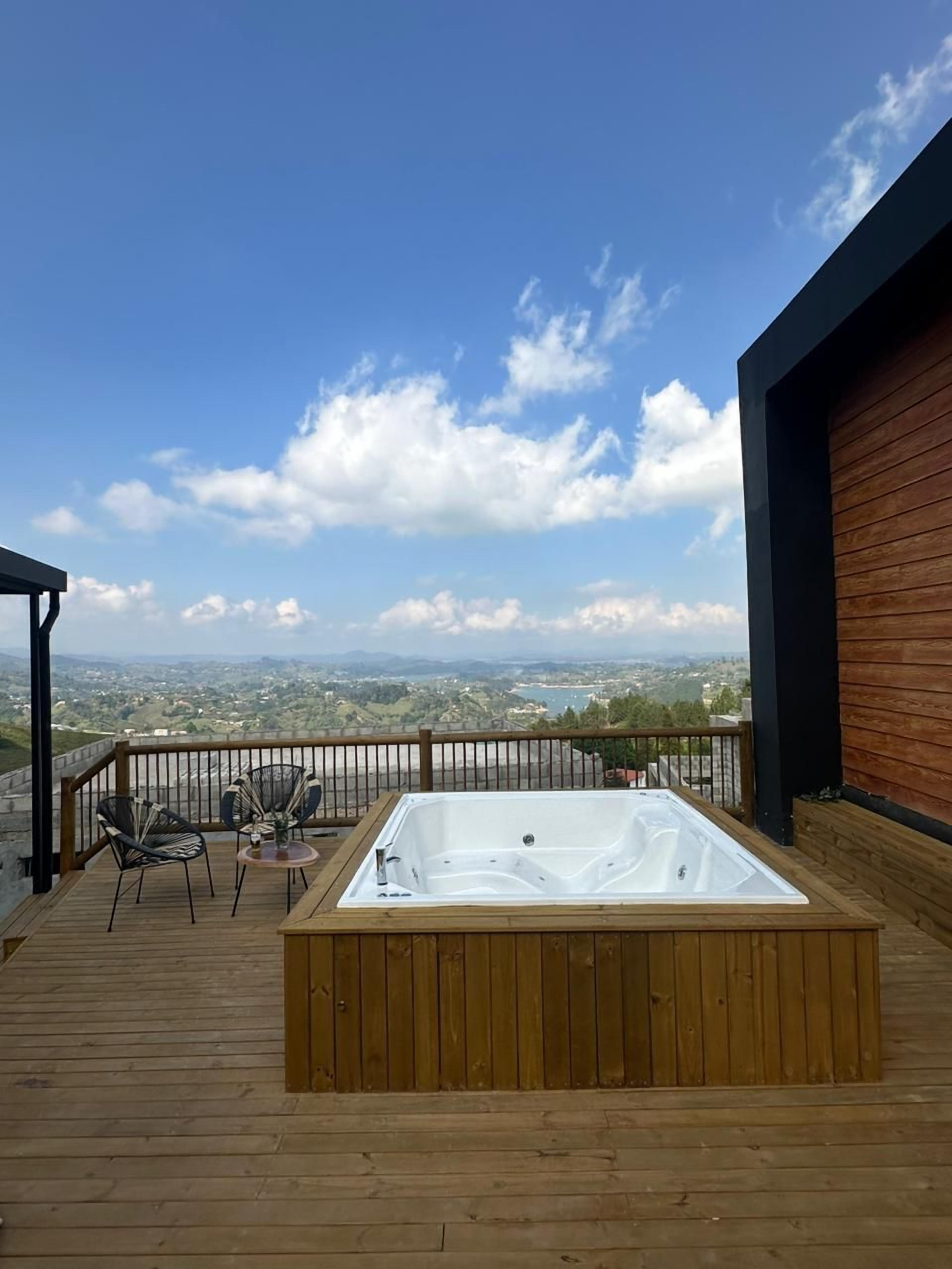 Una terraza de madera con un jacuzzi, dos sillas y una mesa.