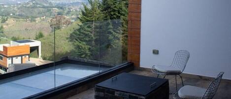 Un balcón moderno con techo de madera, una barandilla de vidrio y vistas a un paisaje montañoso.