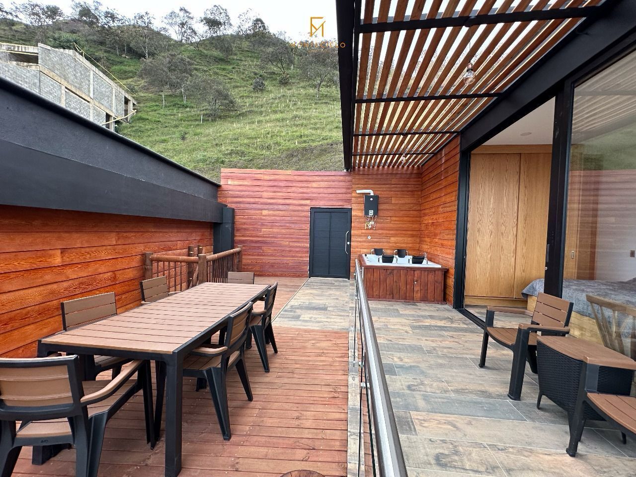Une terrasse extérieure avec une table et des chaises en bois, un barbecue et un sol carrelé en pierre.
