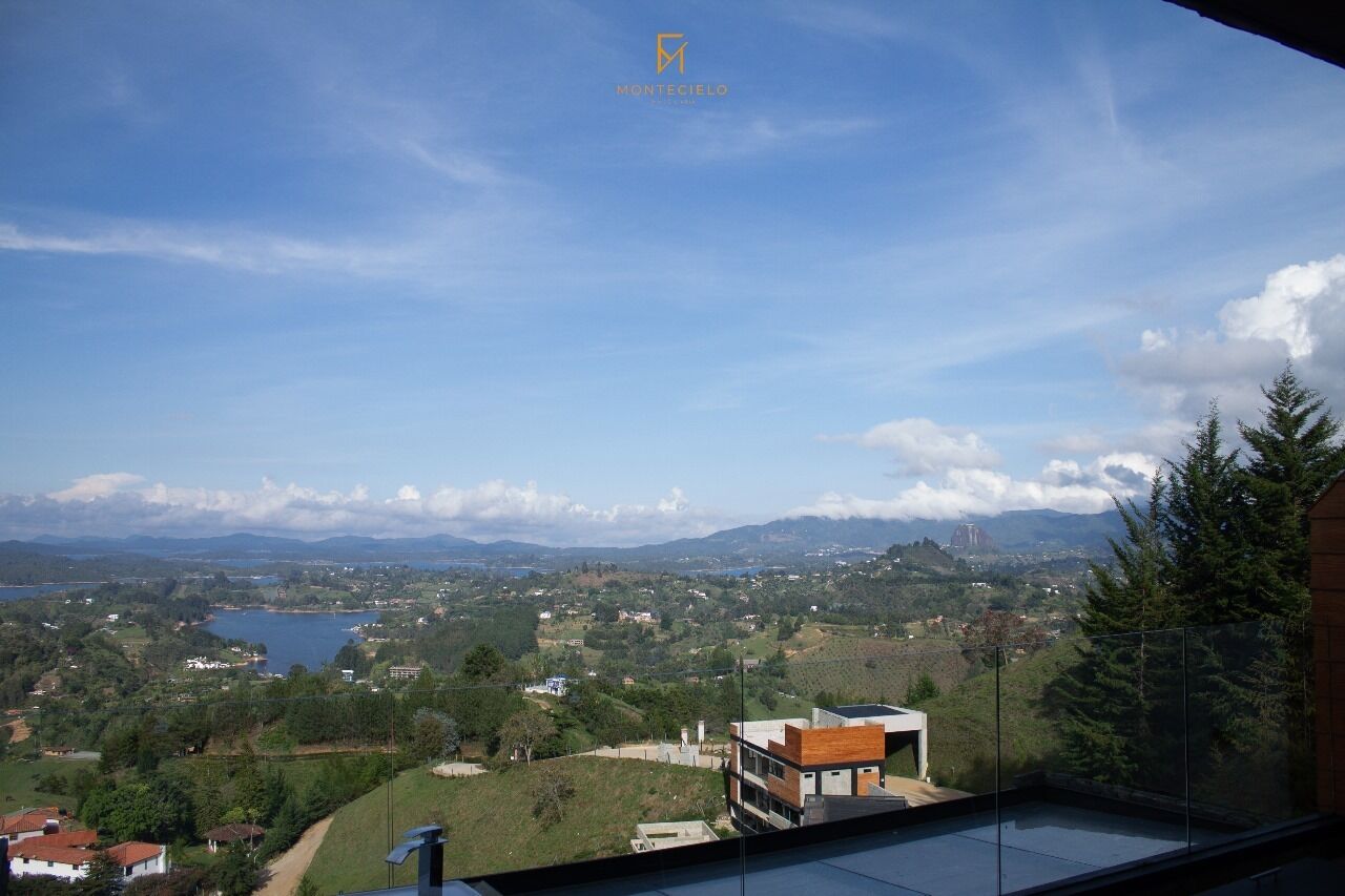 A panoramic view from a balcony overlooking a lake, mountains, and a town.