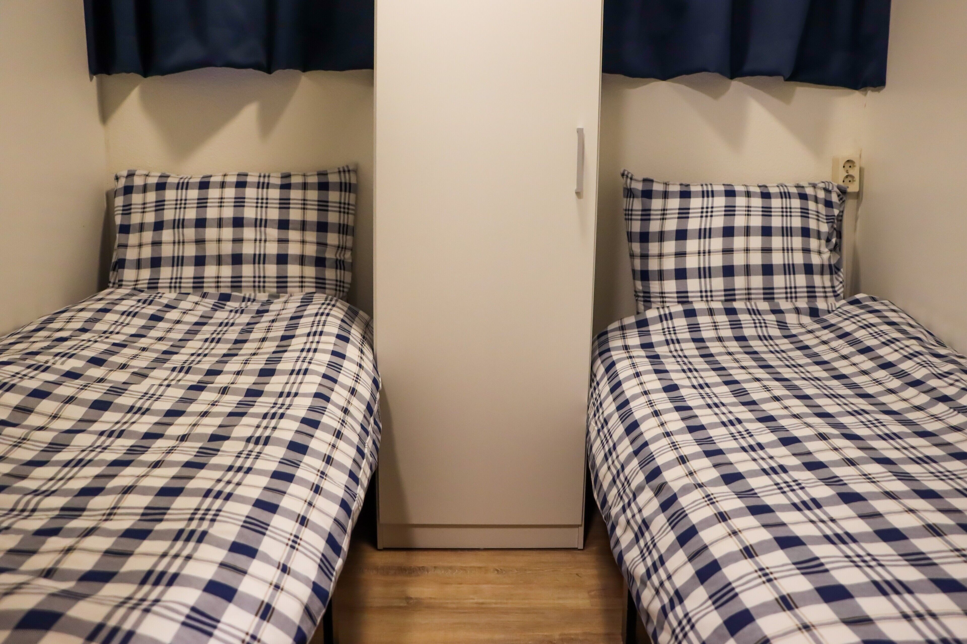 Two single beds with checkered bedding, a wooden floor, and a white door with a handle.