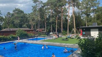 A swimming pool surrounded by tall trees and a grassy area with lounge chairs.