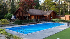 Una piscina junto a una cabaña de madera con un porche cubierto.