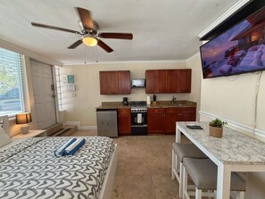 A compact hotel room with a bed, a ceiling fan, a kitchenette, a dining area, and a TV mounted on the wall. - Ocean Breeze Free Parking! Apt 2 (Fort Lauderdale)