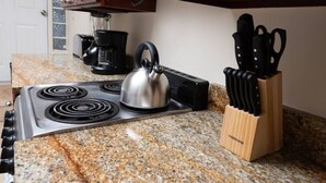 A kitchen with a stove, kettle, coffee maker, and knife block.
