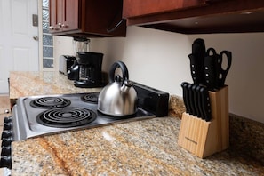 A kitchen with a stove, kettle, coffee maker, and knife block.