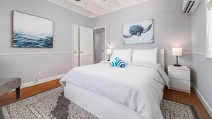 Une chambre à coucher avec un lit, un ventilateur de plafond, un climatiseur fixé au mur et un tableau représentant une tortue.