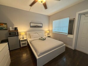 Une chambre à coucher comprenant un lit, des lampes de chevet, un ventilateur de plafond, un four à micro-ondes et une petite table avec une lampe.
