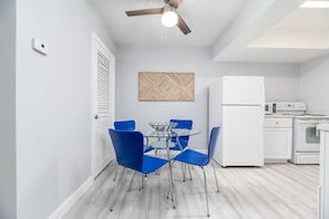 A compact kitchen with a dining area, white appliances, and a ceiling fan.