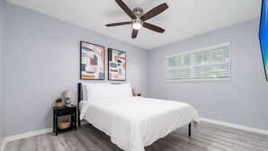 A bedroom with a bed, a ceiling fan, a nightstand, a lamp, and abstract wall art. - Short Walk to Wilton Drive! Apt2 (Wilton Manors)