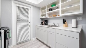 A modern kitchen with white cabinetry, a built-in shelf with kitchenware, a coffee maker, and a sink. - Short Walk to Wilton Drive! Apt2 (Wilton Manors)
