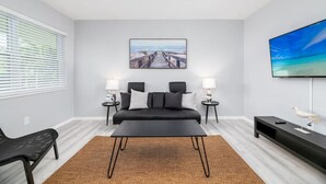 A modern living room with a black sofa, a coffee table, a TV, and a framed picture on the wall. - Short Walk to Wilton Drive! Apt2 (Wilton Manors)