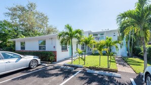 A parking lot with a white car, a building with a red door, and palm trees.