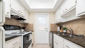 A compact kitchen with white cabinets, a stove, a sink, and a door with a view.