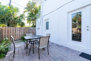 A patio with a table and chairs, a wooden fence, and a white building with a door.